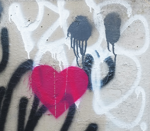 pink heart stenciled onto a concrete support, with a spray paint black happy face beside it