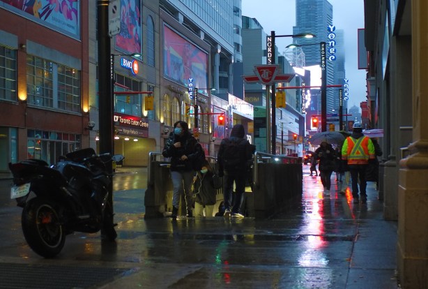 looking north on yonge street, by entrace to TTC subway on sidewalk on east side of yonge street, people coming and going, dark morning, rainy, reflections,
