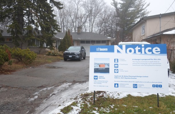 blue and white development notice for Behar planning and design co to redevelopment a section of land on Bayview Ave the involves demolishing a few houses, including large bungalow house behind a large trees still there, sign in the front yards.