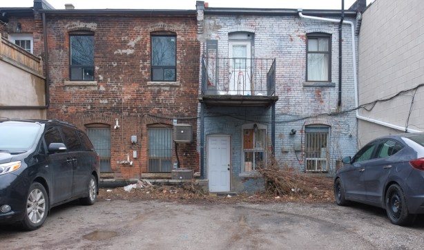 back of two old brick stores on the Danforth, driveways and parking spots, 2 parked cars, small balcony on one