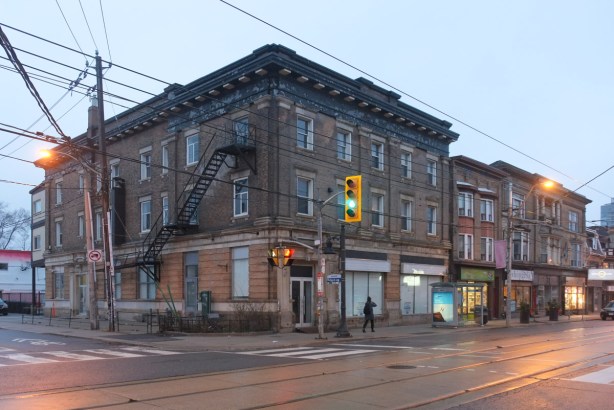 large three storey brick building on the northeast corner of Brock Ave and Queen Street West, stores at street level, traffic lights at the intersection
