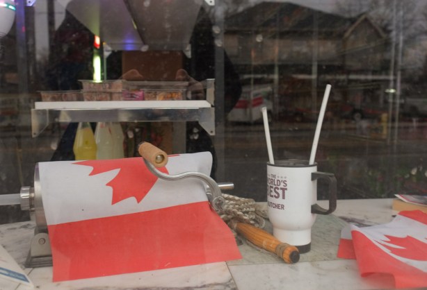 looking in a window that has two Canadian flags, a mug that says best butcher, a hand roller, 