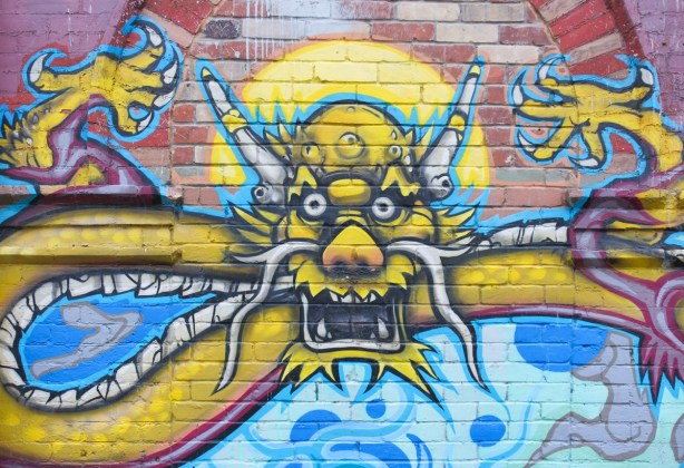 central, gold coloured dragon, looking straight ahead with mouth open, part a larger mural in chinatown with three dragons