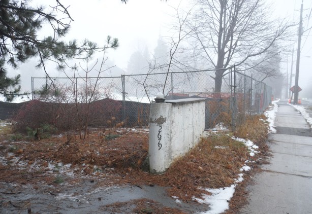 remains of a concrete wall, about 3 feet high, with number 2769 on it, with vacant lot surrounded by chainlink fence in the background 