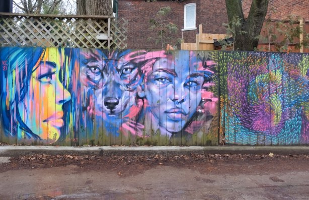 street art on a wood fence, two womens faces, and a wolf, in an alley