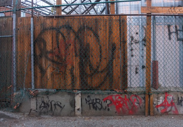 fence in an alley, part chainlink, with old wood, and old metal leaning against it 