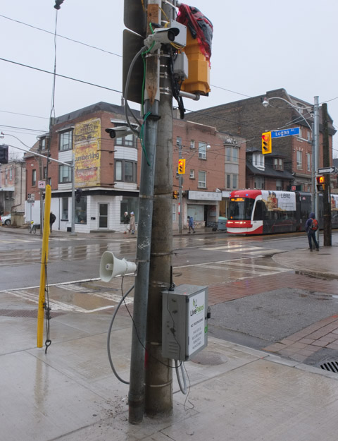 on the northeast corner of Gerrard and Logan is a pole with security cameras and a loud speaker, looking diagonally across to southwest corner, TTC streetcar stopped there 