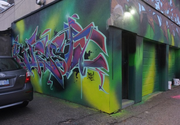 garage in alley behind Queen West, painted in shades of green with a tag throw up piece on one wall 
