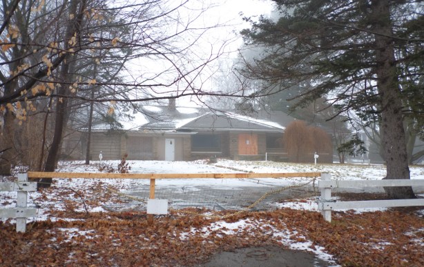 abandoned and empty bungalow with low white fence in front of it, driveway blocked, snow, fog, 