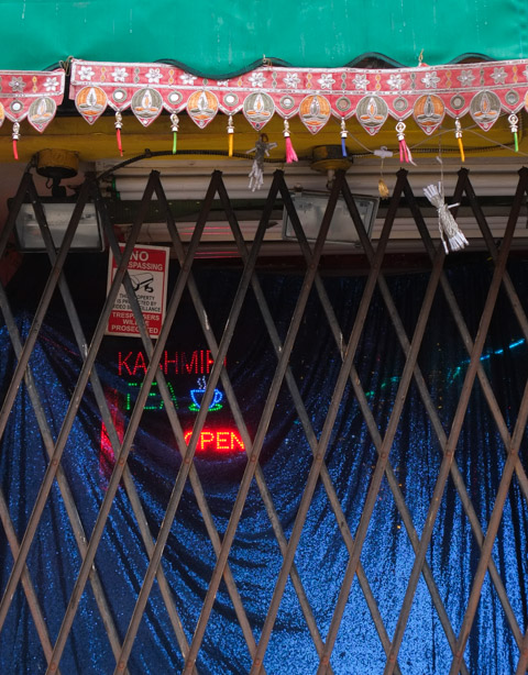 close up of metal grate covering blue curtain over the front window of lahore bbq and paan center