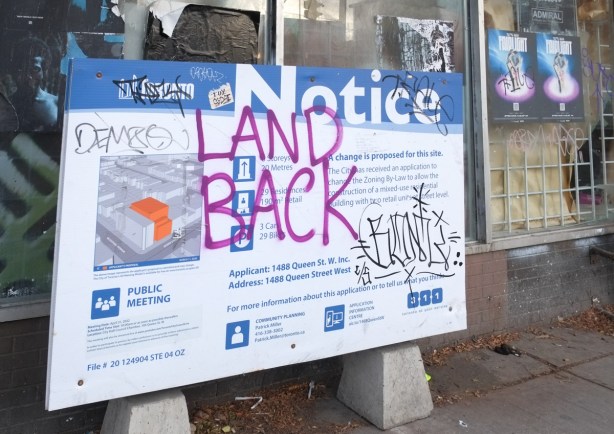 blue and white development notice sign for 1488 queen west, with graffiti land back written on it 