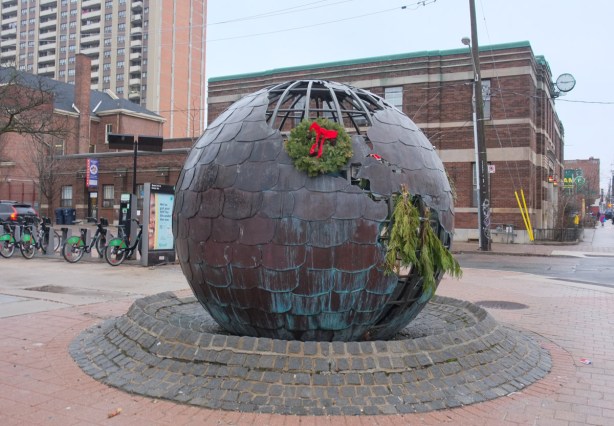 sculpture outside Parkdale Library, a metal globe, with a Christmas wreath on it
