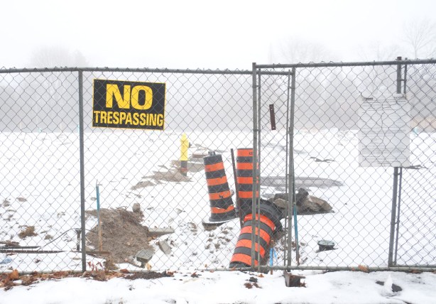 chainlink fence in front of a vacant lot covered by a bit of now, black and yellow no trespassing sign posted on fence, some orange and black cones behind the fence, foggy day 