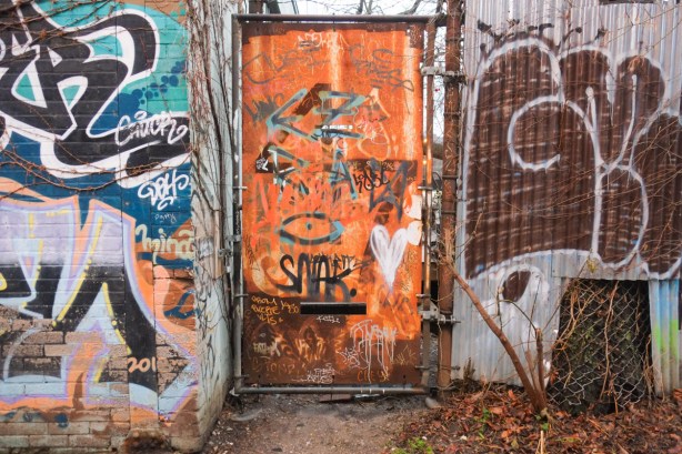 orange rusty metal door in a fence in an alley