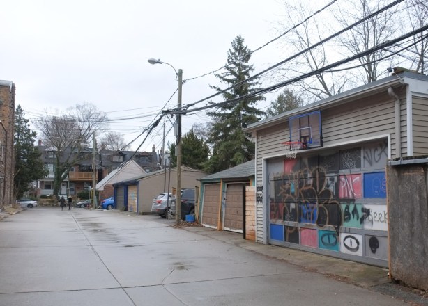 garages in the alley behind Danforth near Bowden including one with a basketball hoop above the door and the squares in the door all painted differently