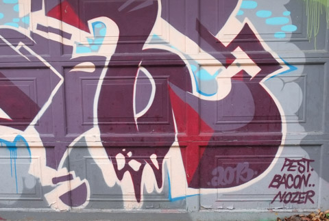 corner of a mural signed pest bacon and nozer, on a garage door in an alley, in reds and purples, in 2013