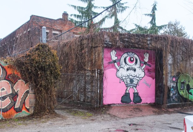 garage covered with dead ivy and a garage door painted pink with a one eyed monsterin black and white