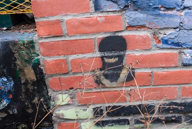 small black stencil, person head and shoulders wearing a black balaclava