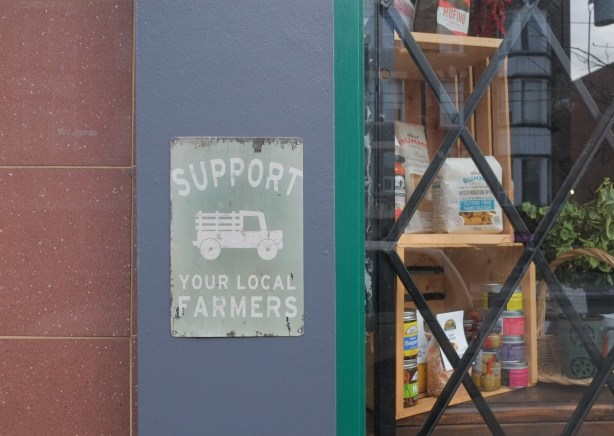 sign beside a store window that says support your local farmers, with a picture of an old fashioned truck 