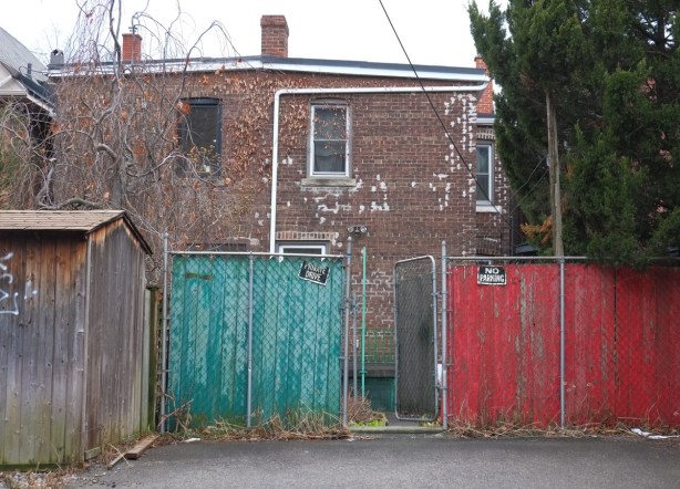 behind an old 2 storey brick house, a fence and a gate. on one side of the gate the fence is painted teal, on the other side it is red 
