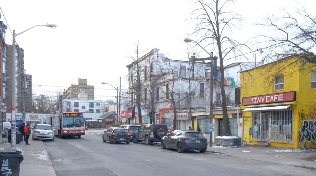 Lansdowne looking south to Queen, yellow building, Tiny Cafe, on the right, people getting on a TTC bus on the left side 