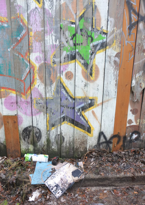 on a wood fence, two stars, old street art, fading and peeling, trash on the dead leaves at the bottom of the fence 