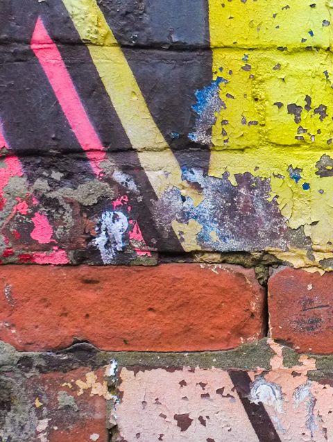 brick wall, paint is peeling, two bricks are entirely exposed 