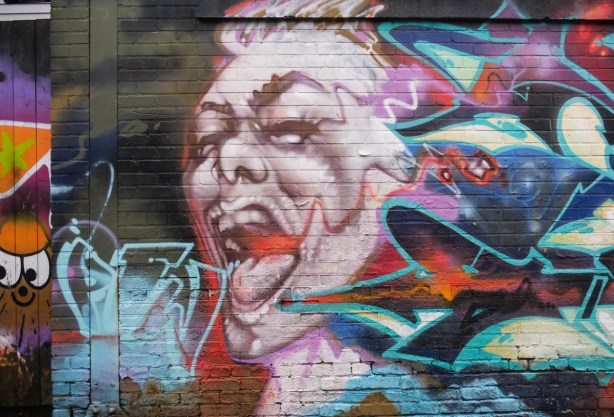 part of a street art mural, a person in brown and beige tones with open mouth, screaming, someone has add a red line coming out of the mouth