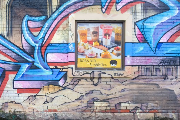 an ad for boba boy bubble tea in an old window, surrounded by street art mural