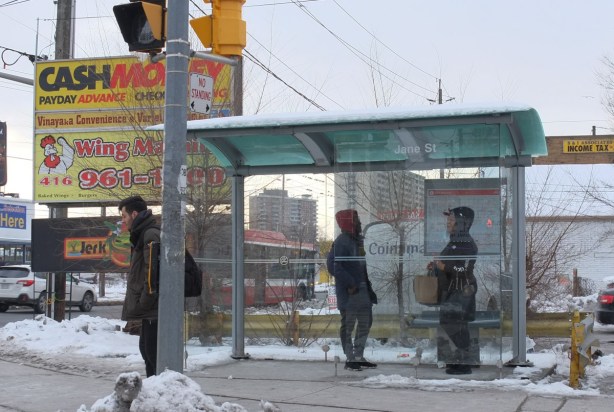two people standing in a bus shelter facing each other, another man is standing outside