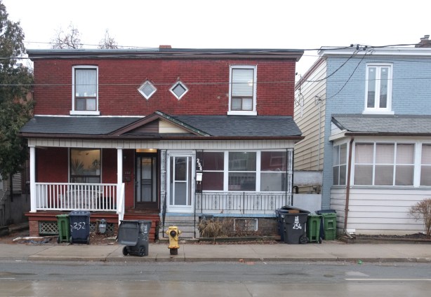 flat roofed seim detached house in fake brick, two small diamond shaped windows in the front, both sides with white porch