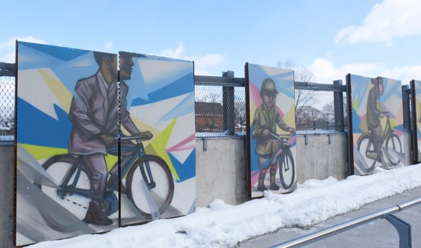 paintings by Elicser elliott of people on bicycles, displayed outside, winter, 
