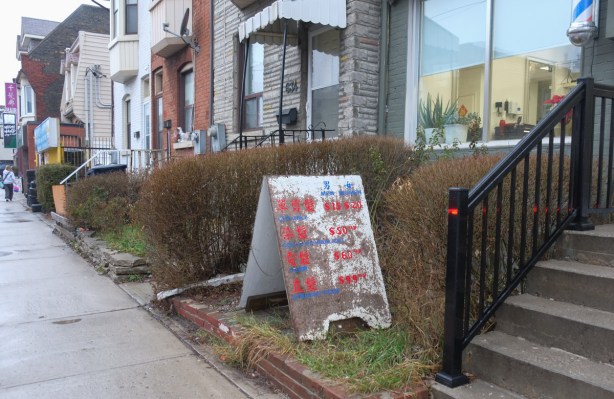 an old weathered sign outside a hair salon on Gerrard Street, red lettering on white but moldy grey