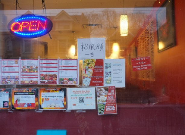 window of a chinese restaurant, orange walls inside, copies of the menu taped to the window, open sign is lit