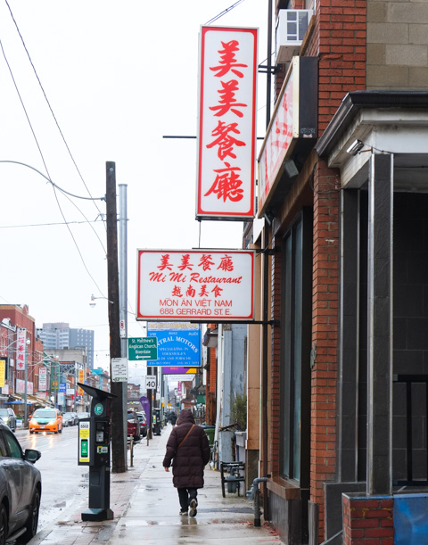a woman walk spast mi mi restaurant on gerrard street 