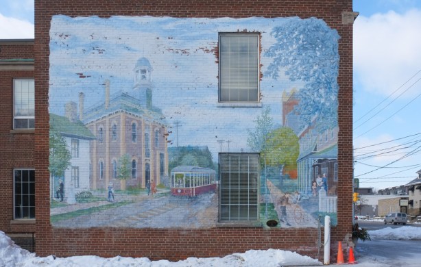On side of 2 storey brick building, a large historic mural by Mario Noviello, Weston Streetscape circa 1900, streetcar, Weston City Hall, Central Hotel, and a church