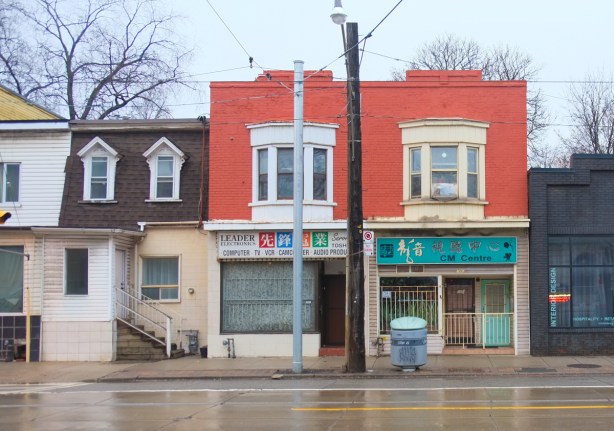 row houses, square roofline, two storey, orange brick upper, bay windows, stores on ground level, 