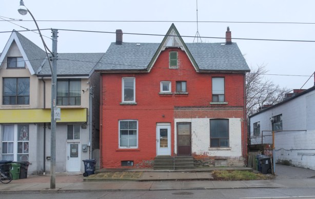 red semi detached house on gerrard with pointy roof in the center, one side has built an enclosed porch by the front door 