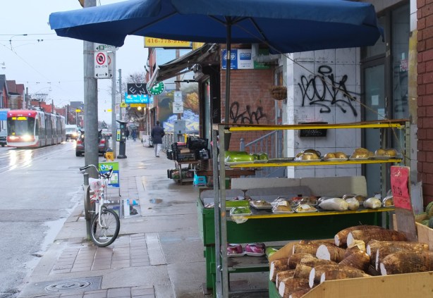 under a blue awning, shelves of plastic wrapped fruits and vegetables for sale
