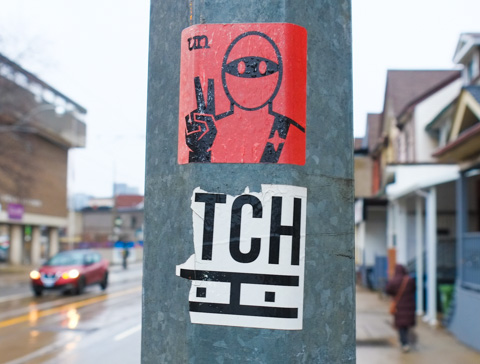 red urban ninja squadron t bonez sticker on a grey metal utility pole, giving peace sign 