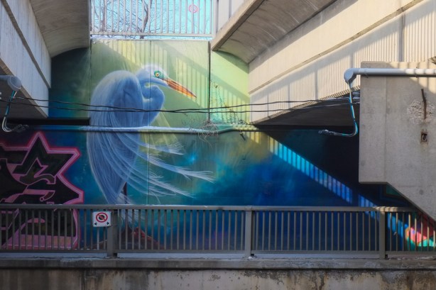 large white bird, crane, with long orange beak, image in a mural under a bridge, 