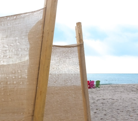 coloured muskoka chairs on the beach, with burlap fence in the foreground