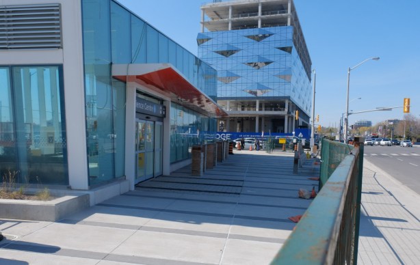 west side of Don Mills Road at Eglinton, new glass covered building on north side is partially completed, new science centre station entrance behind metal fence on south side
