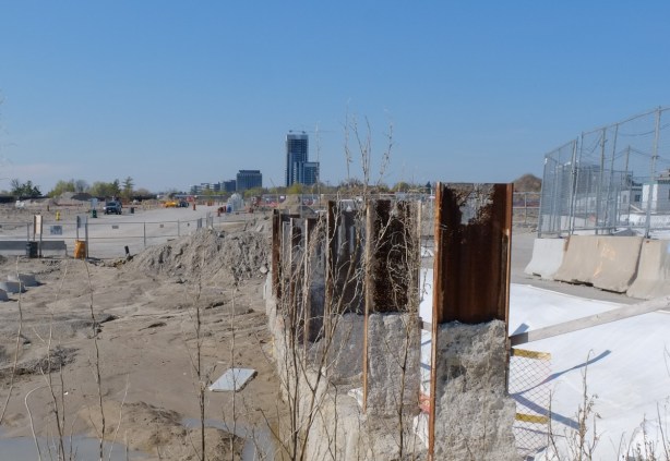 construction site, steel girders slightly rusted upright into the ground, some water puddles, sand and dirt, start of a new street