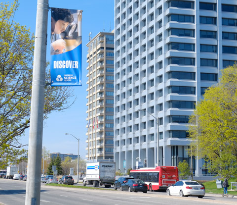 Ontario Science Centre banner on a pole on Don Mills Road with traffic and larger buildings in the background