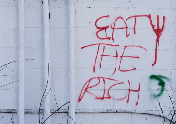 graffiti, red writing on white wall that says eat the rich
