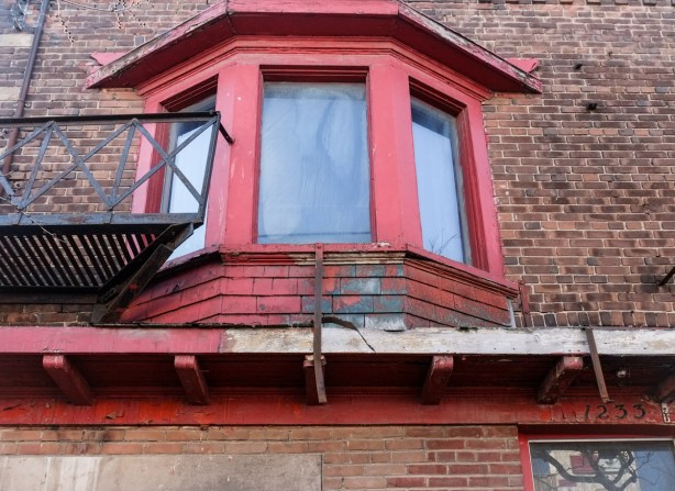 front bay window of 1233 Queen East, red window frame, brown brick building, empty, soon to be demolished