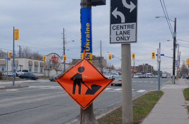 bent orange and black construction zone sign, on a hydro pole on Lawrence, also a yellow and blue slava Ukraine pole wrapper