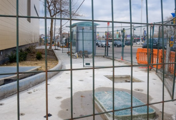 metal construction fence around a newly widened sidewalk with bus shelter in the middle