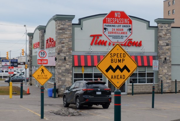 speed bump ahead sign by parking lot of Tim Hortons, also a no trespassing sign